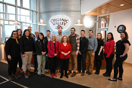 A group of people smile and pose in front of an Organic Valley logo.