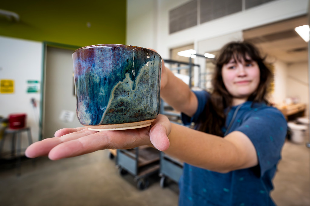 A woman holds out a blue and green glazed mug.