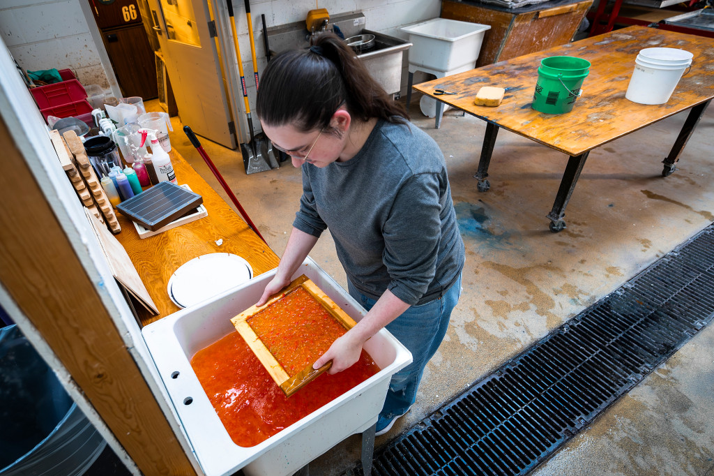 A woman dips a screen into a red liquid in a tray.