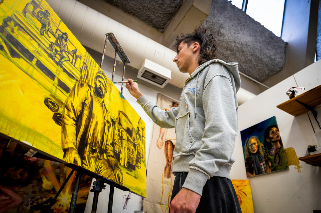 A man uses a brush to put the finishing touches on a yellow painting of a man.