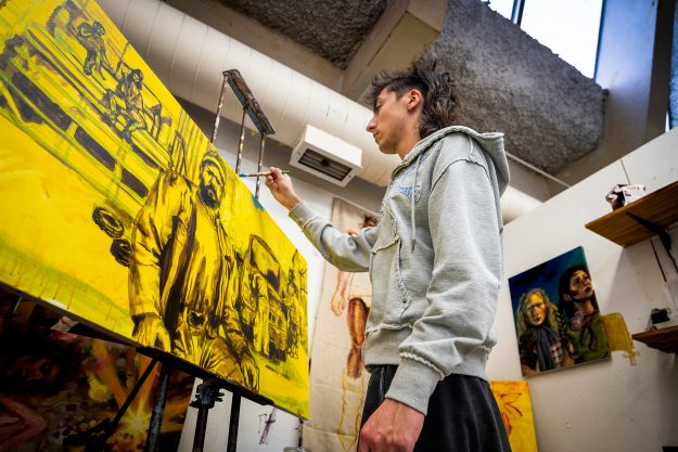 A man uses a brush to put the finishing touches on a yellow painting of a man.