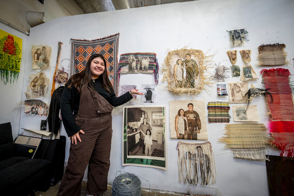 A woman stands in front of a wall decorated with numerous artworks, most in a beige and brown color.