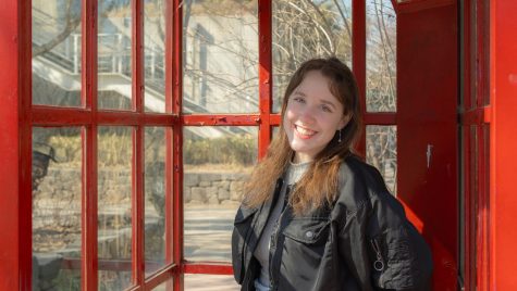 A woman is shown in a telephone booth painted red, with a building visible in the background.