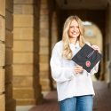 A woman in a white sweater holds a commencement cap with a University of Wisconsin logo on it.