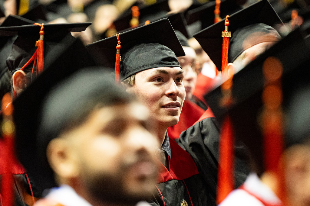 People wearing graduation gowns and caps listen.