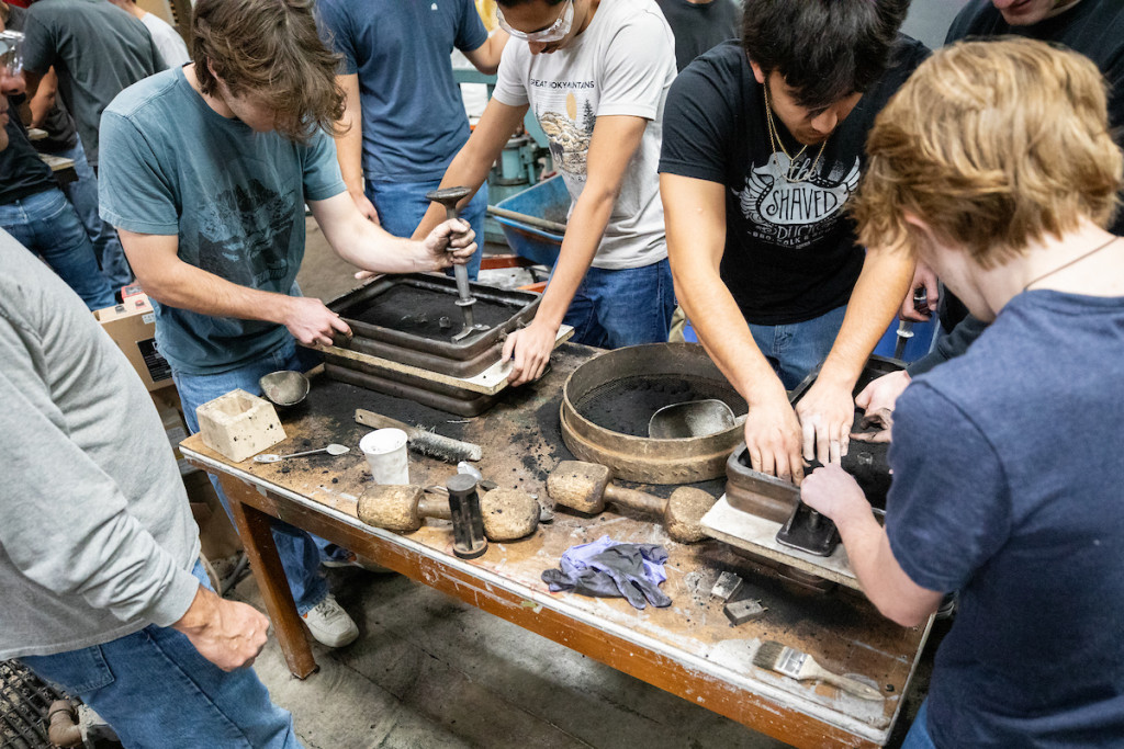 Students are seen working together around a table with equipment on it.