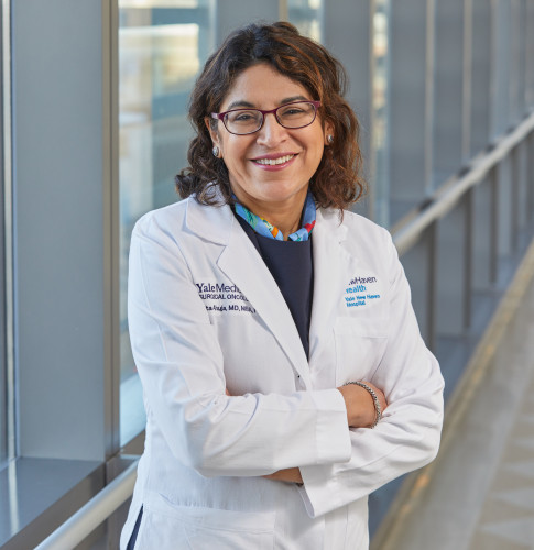 A woman in a white doctor's coat stands, arms folded across her chest, smiling at the camera.