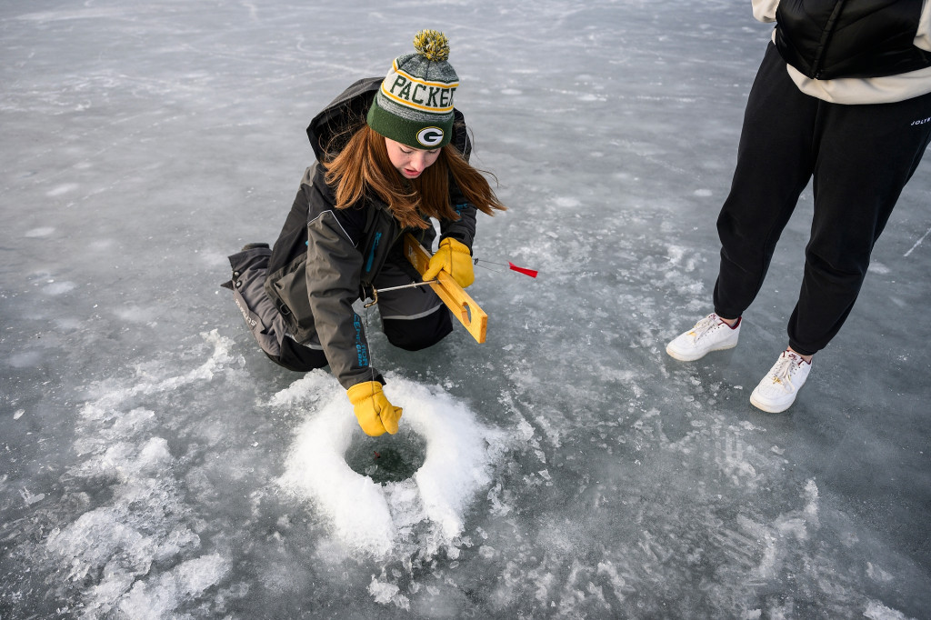 A woman pulls a line out of a hole in a frozen lake.