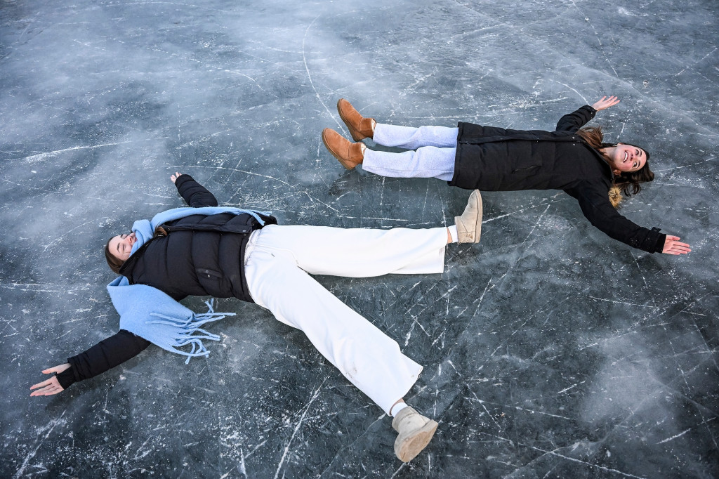 Photo of two people lying on the ice pretending to make snow angels.