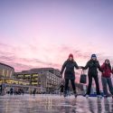 Photo of several people walking on an iced over lake with a colorful sunset behind tehm.