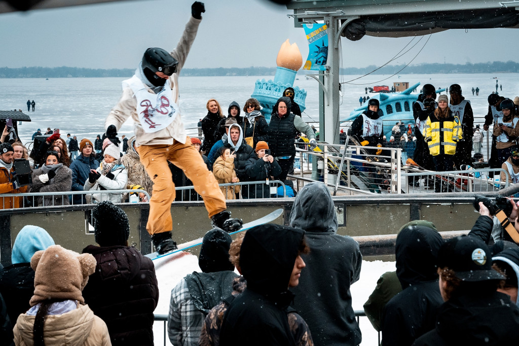 A photo of a snowboarder going off a jump in front of a crowd.