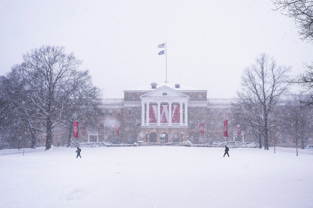 A distant picture shows two students crossing in front of a snow Bascom Hall.